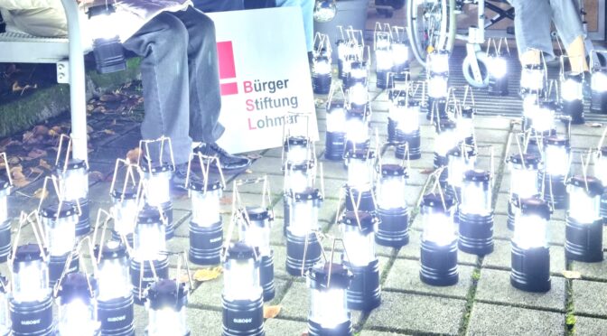 Bildausschnitt des Bildes vom Probelauf der von der Bürgerstiftung Lohmar gespendeten Tischlampe. Zu sehen sind viele leuchtende Tischlampen auf dem Boden der Terrasse vor dem Ev. Altenheim Lohmar mit dem Schild der Bürgerstiftung Lohmar.